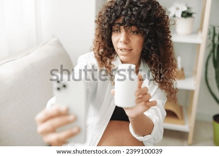Pregnant woman blogger with a jar of pills and vitamins sits on the couch at home and takes pictures of herself on the phone, maintaining pregnancy and replenishing vitamins and minerals