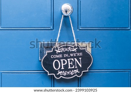 The inscription on a black sign on a blue door - come in, we are open