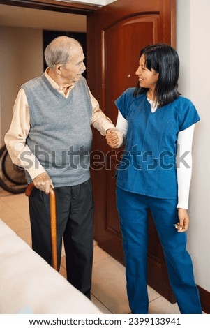 Vertical photo of a nurse holding hand of an elder man while walking indoors at home