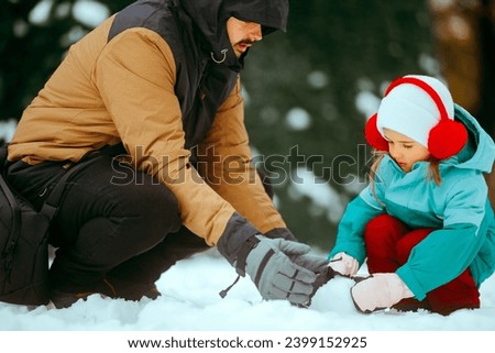 
Father and Daughter Playing in the Snow Making a Snowman 
Dad and little girl building a huge snowball together
