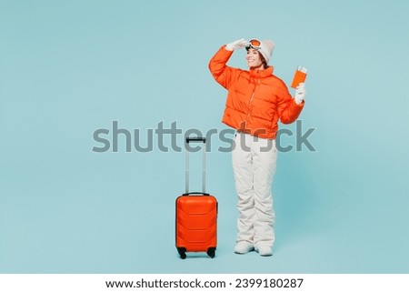 Traveler skier woman wearing padded windbreaker jacket ski goggles mask hold passport ticket bag isolated on plain blue background Tourist travel abroad in free time rest getaway. Air flight concept