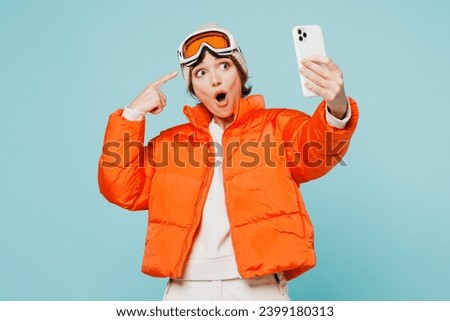 Skier young woman wearing padded windbreaker jacket hat ski point goggles mask do selfie shot mobile cell phone travel rest spend weekend winter season in mountains isolated on plain blue background
