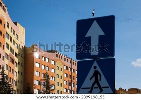 a road sign above which you can see a person walking on a tightrope in the distance