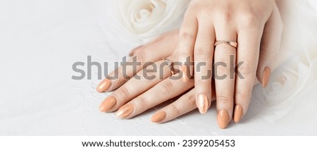 Beautiful female hands with fresh Peach Fuzz trendy color manicure lying on backdrop with white rose flowers . Wedding or spa or celebration soft background with copy space. Royalty-Free Stock Photo #2399205453