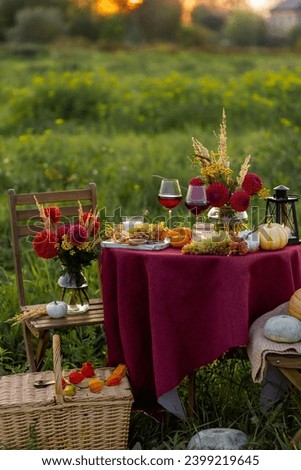Beautiful elegant outdoor romantic dinner table decor countryside style: pumpkins, candles, flowers, red wine, gourmet cheese board. Cozy garden interior, open air party event. Sunset golden hour Royalty-Free Stock Photo #2399219645