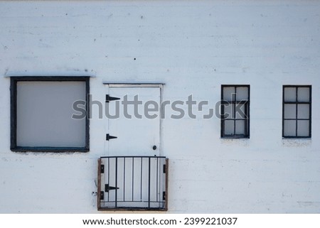 A photo of a rundown white brick building with an unusable door. 
