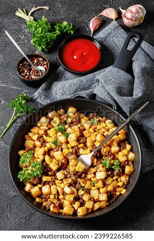 Beef Hash with roasted corn, garlic and parsley on a skillet with fork on concrete table with grey cloth and ketchup, vertical view from above Royalty-Free Stock Photo #2399226585