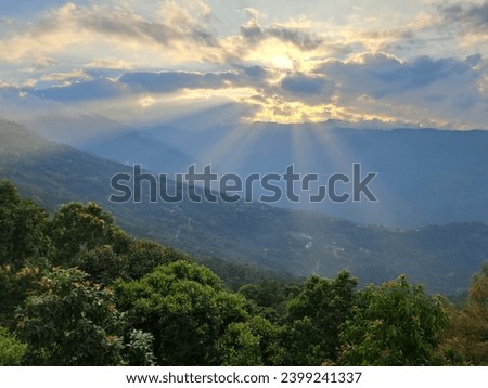 The picture is taken at sunset in the mountains.The rays are coming from behind the clouds. In contrast to the sunrays the greenery below is making a heavenly view.