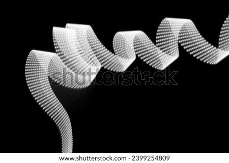 White neon curved wave of light as curls or swirl with dotted stripes on black background. Abstract background with motion light effect, light painting in New Year style.