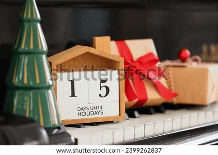 Calendar with text 15 DAYS UNTIL HOLIDAYS, Christmas gifts and decor on piano keys, closeup
