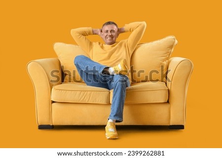 Mature man resting on sofa against yellow background