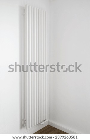 Vertical radiator install on white wall in empty room with minimalist interior design. Home or apartment with modern central heating system. Responsible consumption of resources for comfort living Royalty-Free Stock Photo #2399263581
