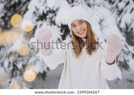 Happy woman in knitted white clothes holding snowflakes on the background of a snowy pine tree in winter