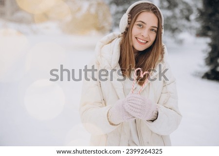 A cute girl in knitted mittens holds candy canes in the form of a heart in winter park