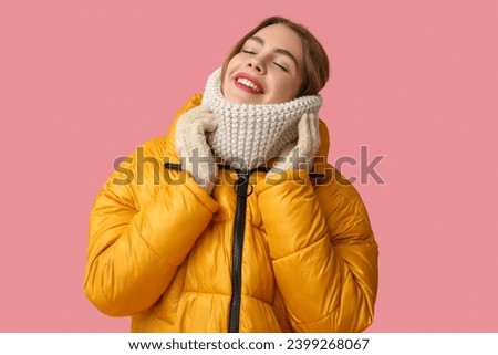 Beautiful young woman in warm winter clothes on pink background
