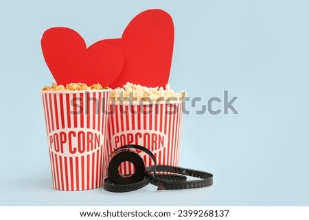 Buckets of popcorn with paper hearts and film reel on blue background. Valentine's Day celebration