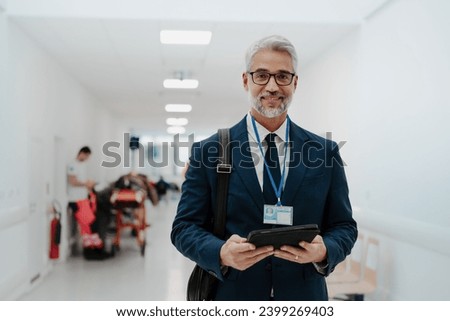 Portrait of pharmaceutical sales representative in medical building, waiting for doctor, presenting new pharmaceutical product. Smiling drug rep standing in hall holding tablet. Royalty-Free Stock Photo #2399269403