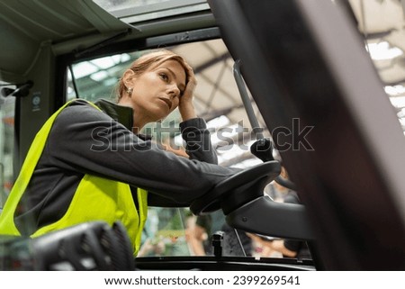 Female forlklift driver feeling overwhelmed from amount of work. Tired, exhausted warehouse worker preparing products for shipmennt, delivery, checking stock in warehouse. Royalty-Free Stock Photo #2399269541