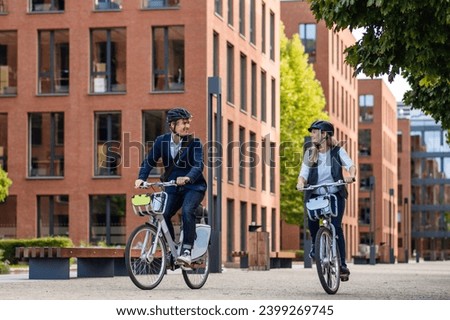 Spouses commuting through the city, riding bike on street. Middle-aged city commuters traveling from work by bike after a long workday. Royalty-Free Stock Photo #2399269745