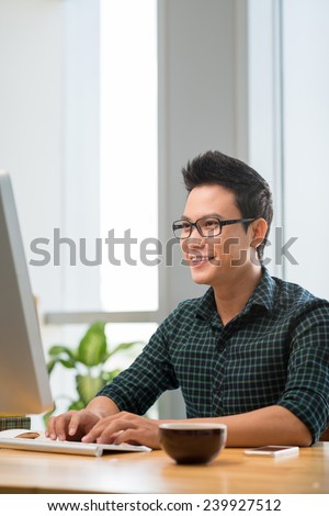 Smiling Vietnamese man working on computer indoors