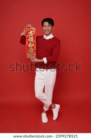 Happy Chinese new year. Asian man holding greeting couplets isolated on red background. Chinese text means May you have happiness and prosperity.