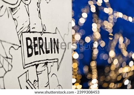 Berlin's artistic allure: A white wall adorned with a black illustration and 'Berlin' signage resembling a pointer, revealing a vibrant scene of glowing yellow lights beyond.