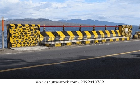 
yellow and black bridge fence on the edge of the road. with a clear blue beach background
