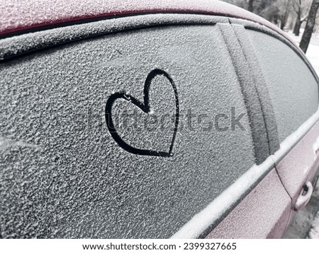Heart shape hand drawing on the thin snow surface covers on the windows of the car. Clean and care for automobile vehicles in the frosty cold winter season outdoor.
