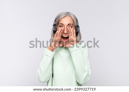 middle age woman feeling happy, excited and positive, giving a big shout out with hands next to mouth, calling out. music concept