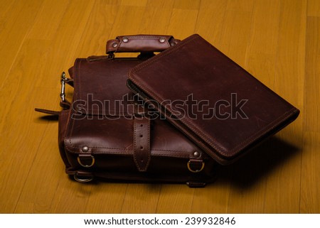 Brown, worn leather briefcase and portfoilo on a hardwood floor