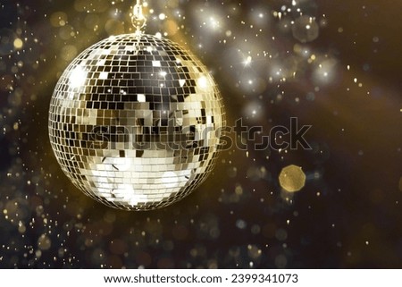 Shiny disco ball under golden lights on dark background, space for text. Bokeh effect