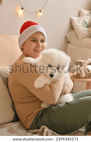 Christmas at home. Small children in a Santa hat hug a pet and open Christmas presents. Celebrating winter holidays. happy new year. Samoyed dog