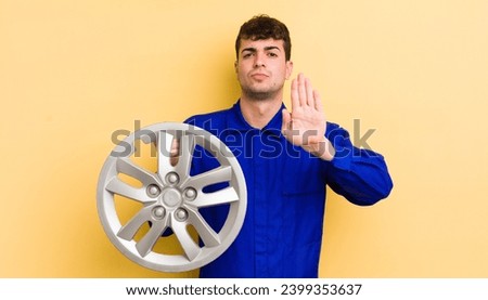young handsome man looking serious showing open palm making stop gesture. car repairman concept