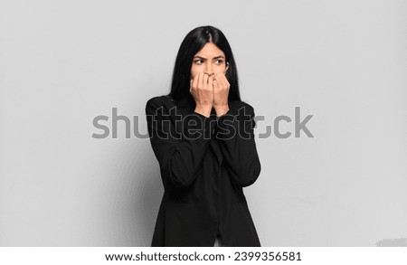 young hispanic businesswoman looking worried, anxious, stressed and afraid, biting fingernails and looking to lateral copy space
