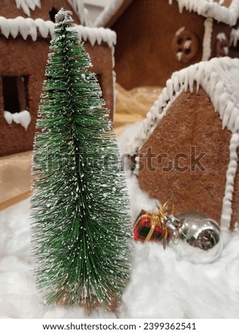 Christmas theme picture of house made cinnamon cake and its decoration of tree, silver balls, snow and red present