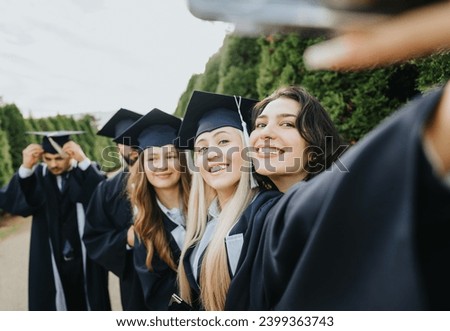 Celebrate graduation with friends in a park. Students in gowns and caps creating memories, taking selfies together. Happy graduates have achieved a successful bachelors degree.