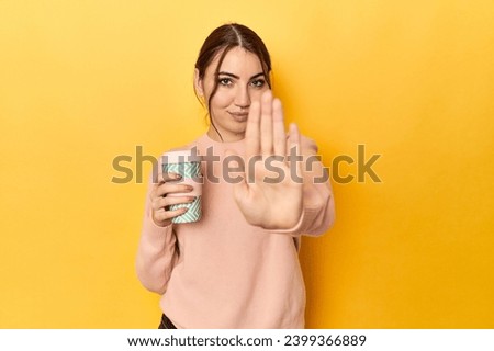 Young caucasian woman holding a takeaway coffee cup standing with outstretched hand showing stop sign, preventing you.