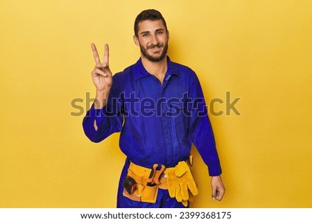 Young Hispanic man in a blue jumpsuit Young Hispanic man in a blue jumpsuitjoyful and carefree showing a peace symbol with fingers. Royalty-Free Stock Photo #2399368175