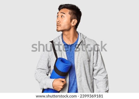 Young Chinese athlete with a yoga mat prepared for practice in studio