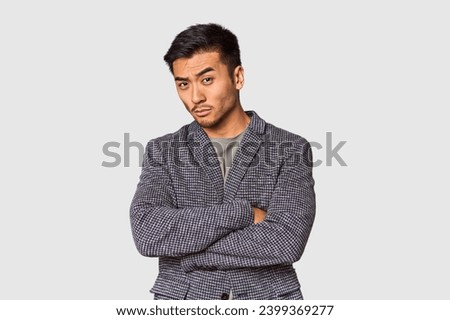 Young Chinese man in studio background suspicious, uncertain, examining you.