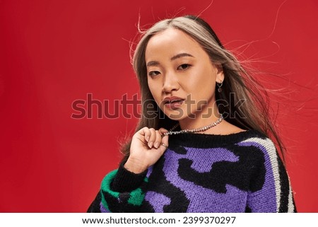 beautiful young asian woman with dyed hair in vibrant sweater with animal print touching necklace