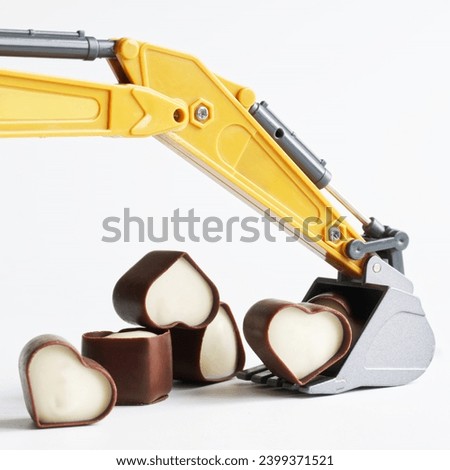 Toy excavator bucket with heart-shaped chocolates. Concept of mining and choosing a love partner, creating a family, dating site. White background. Photo. Close-up
