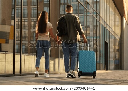 Long-distance relationship. Young couple with luggage walking near building outdoors, back view Royalty-Free Stock Photo #2399401441