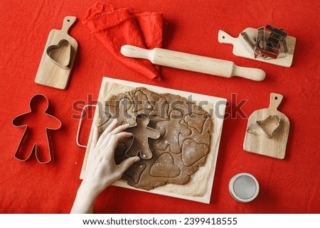 Top view preparing Cooking ginger cookies, Christmas and New Year traditional cookie in shape of gingerbread man, raw rolled out dough, woman hands holding metal pastry cutter on dough, above flat lay