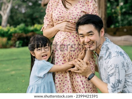 a man and a little girl was kissing the stomach of a pregnant lady outside the park in a bright sunny setting