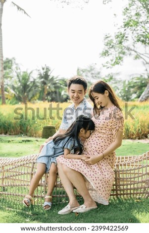 A family consisting of 3 that were father, a pregnant mother and a girl are enjoying their picnic in the park under the afternoon sunlight. They walked, kissed and expressed happiness and joy 