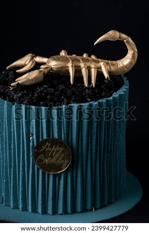 Cake with turquoise chocolate icing in the shape of corrugated paper decorated with edible golden scorpion on top. Birthday cake for a Scorpio sign of the zodiac on the black background