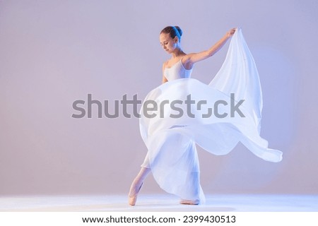 young ballerina in pointe shoes dances in long flying white skirt on a white background Royalty-Free Stock Photo #2399430513