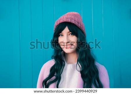 Stylish young smiling hipster woman with color hair wearing pink coat and knitted hat on turquoise green wooden background. Urban seasonal city street fashion. Barbiecore style. Selective focus. Royalty-Free Stock Photo #2399440929