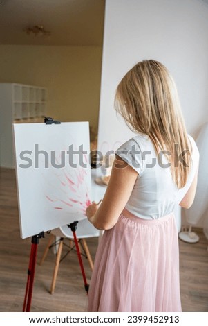 Young woman artist with palette and brush starts to paint abstract pink picture on canvas at home. Art and creativity concept. High quality photo